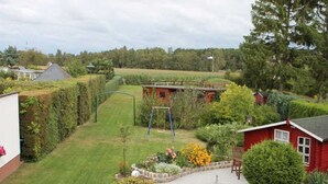 Un immobile residenziale con un prato curato, altalene, un piccolo giardino fiorito e un edificio rosso.