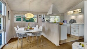 Een moderne keuken met een centraal eiland, witte keukenkastjes en een eethoek met een witte tafel en stoelen.