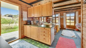 A wooden cabin with a kitchen area featuring wooden cabinets, a sink, and a coffee maker. There is a dining area with a table and chairs, and a large window offering a view of the outdoors.