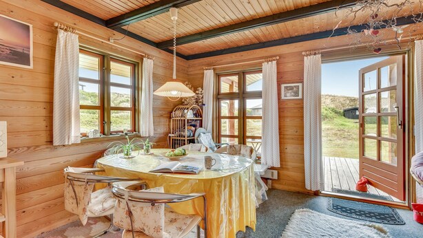 A cozy cabin interior with a round dining table, wooden walls, and large windows offering a view of the outdoors.