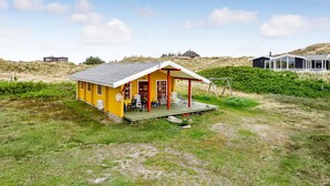 A yellow house with a porch, surrounded by grass and dunes.