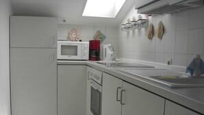 Una cocina compacta con gabinetes blancos, un microondas, una cafetera y un lavamanos.