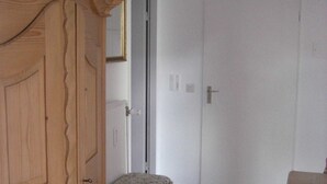 Una habitación con un armario de madera, un banco con un cojín estampado y suelo de baldosas.