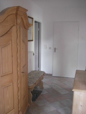 Een kamer met een houten garderobe, een bank met een gestreept kussen en een betegelde vloer.