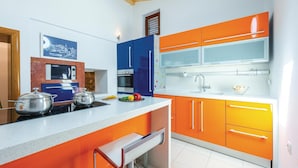 Una cocina moderna con gabinetes naranja, encimera blanca y electrodomésticos de acero inoxidable.