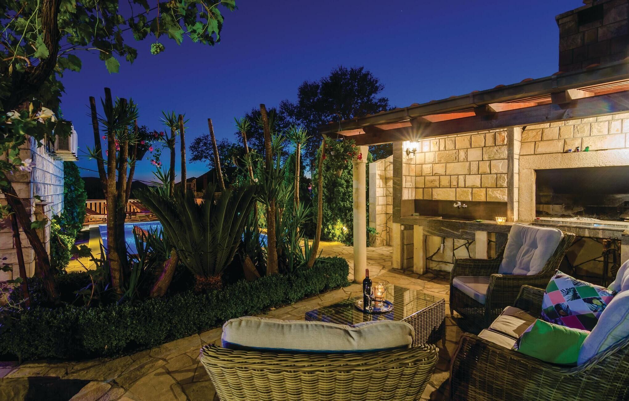 An outdoor patio with wicker furniture, a stone fireplace, and a pool in the background.