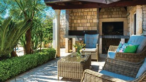 Un área de estar al aire libre con muebles de mimbre, una chimenea de piedra y una pérgola.