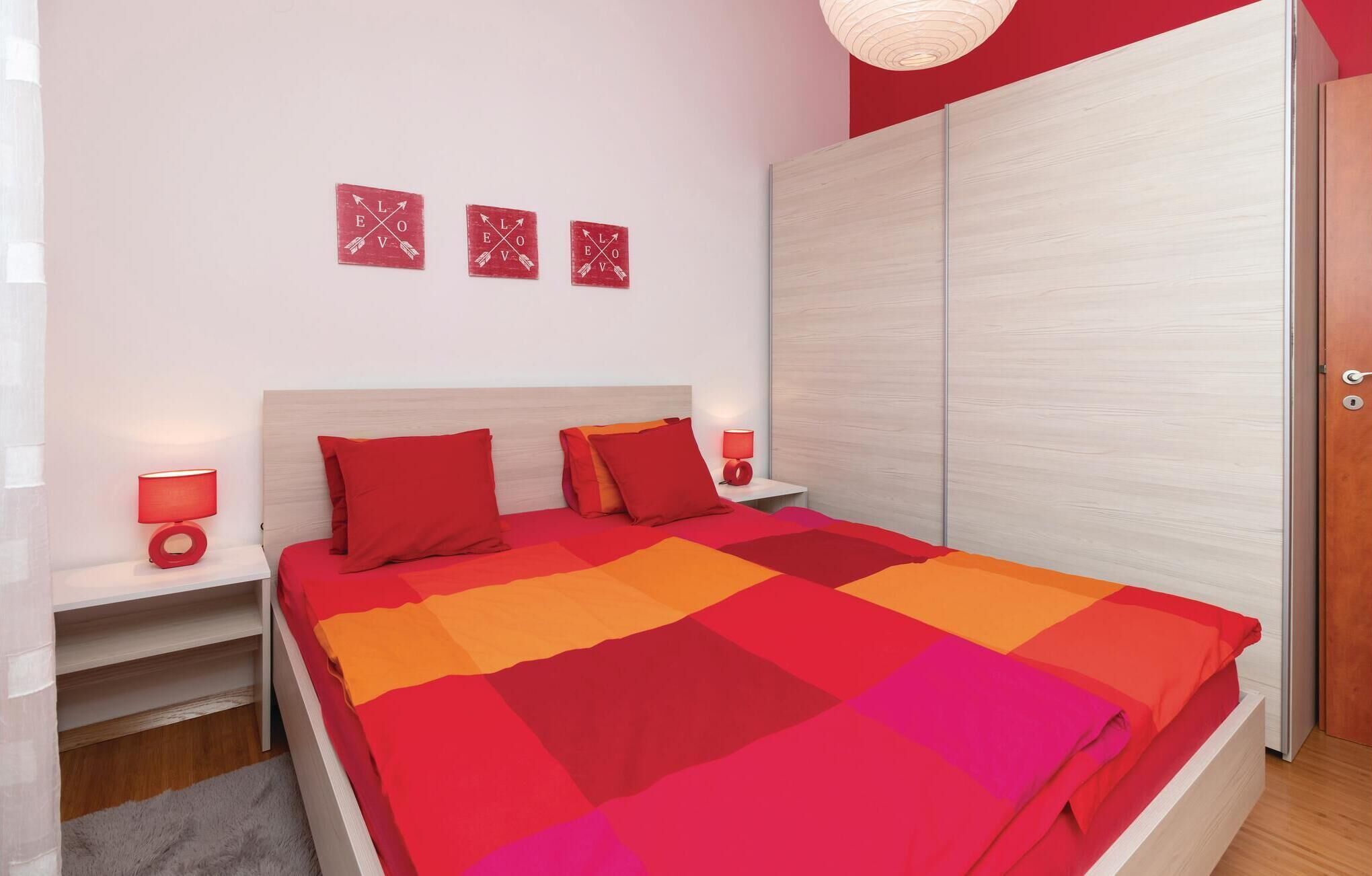 A bedroom with a bed, two bedside tables with lamps, a wardrobe, and three wall decorations.