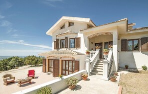 Una casa de dos pisos con balcón, plantas en macetas y muebles de exterior.