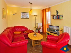 A living room with a red leather sofa, a wooden coffee table, a TV, and a bookshelf.