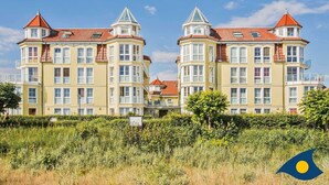 Un bâtiment jaune, doté de nombreuses fenêtres et surmonté de toits rouges, entouré de verdure.