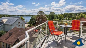 Un balcon avec deux chaises à carreaux rouges et une petite table, d’où l’on peut admirer un lac et les bâtiments environnants.