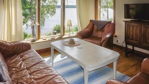 Un salon avec un canapé en cuir marron, une table basse blanche et un fauteuil en cuir marron. On y trouve un téléviseur posé sur un meuble en bois, ainsi qu’une fenêtre donnant sur un plan d’eau.
