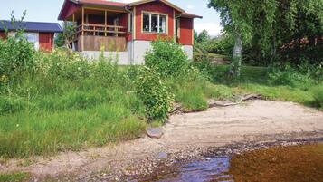A house with a porch, surrounded by greenery and a small stream.