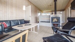 Un salon moderne avec un canapé en cuir noir, une table basse blanche et un fauteuil en cuir noir. On aperçoit un foyer avec une façade en verre au fond.