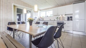 Une cuisine moderne avec des meubles blancs, un four en acier inoxydable et un réfrigérateur noir. On y trouve une table à manger avec quatre chaises, et une plante en pot posée dessus.