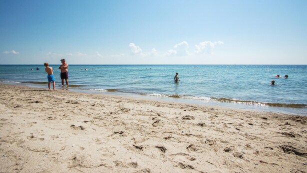 Une plage où l’on voit des gens nager et se tenir debout sur le sable.