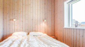 Une chambre avec un mur lambrissé en bois, un lit avec une literie blanche, deux lampes fixées au mur et une fenêtre donnant sur l’extérieur.