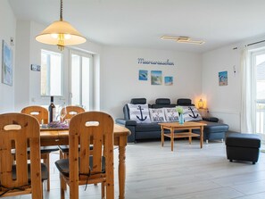 Ein modernes Wohnzimmer mit Essbereich, ausgestattet mit einer Couch mit ankerförmigen Kissen, einem Holztisch und einer Pendelleuchte.