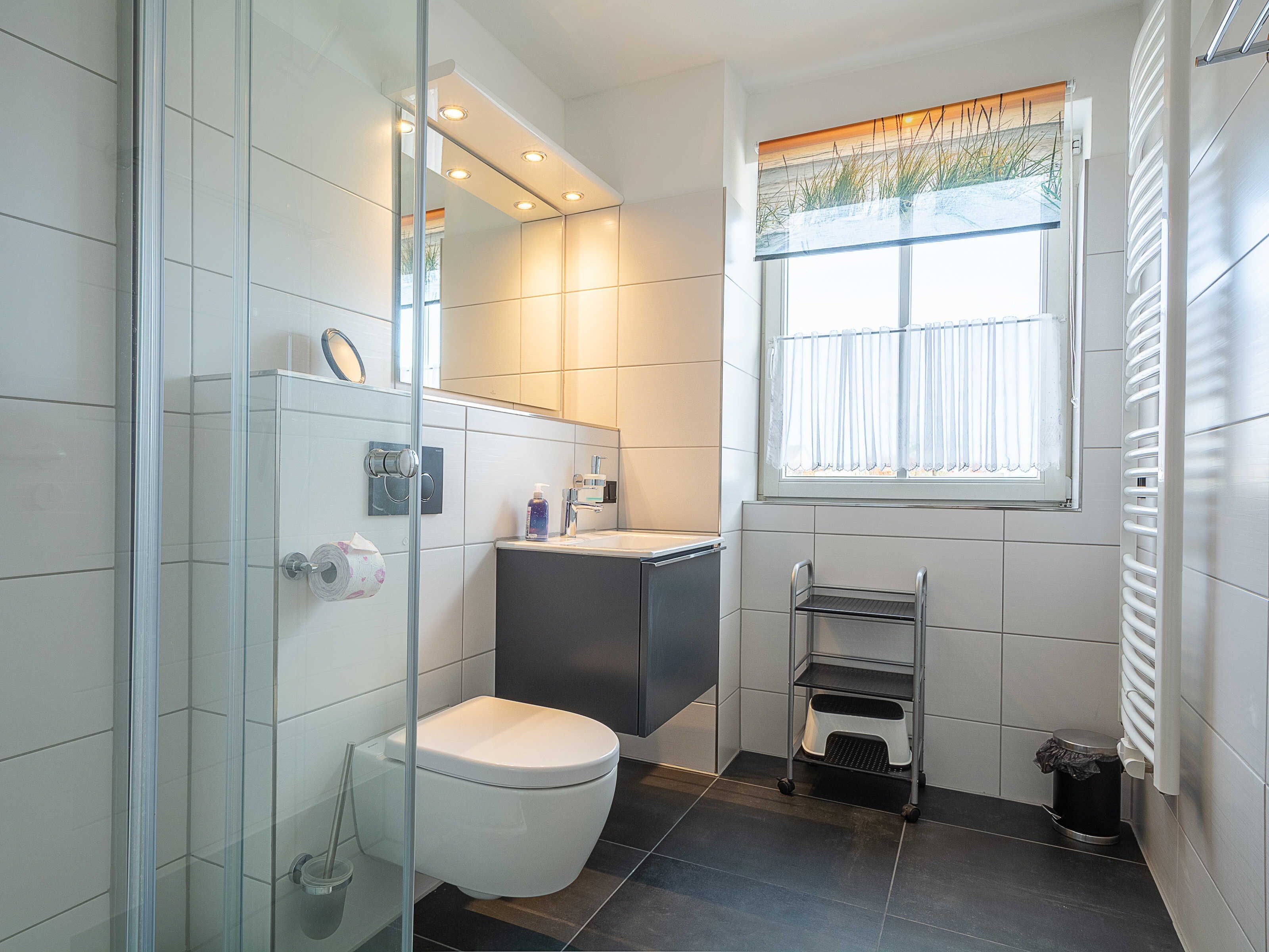 A modern bathroom with a glass shower enclosure, a toilet, a sink with a vanity, and a window with a view of grass.