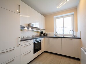 Eine moderne Küche mit weißen Schränken, einem eingebauten Backofen, einer Kaffeemaschine und einem Fenster mit Aussicht.