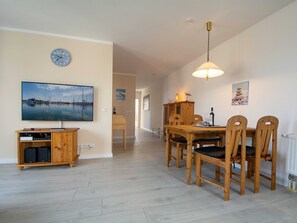 A dining area with a wooden table and chairs, a television mounted on the wall, and a clock. - At the city forest Whg 15-14 .. - 15-14 (Kühlungsborn)