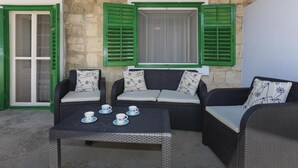 Un coin salon avec des meubles en osier, une table avec des tasses et une fenêtre avec des volets verts.