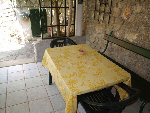 A table with a yellow floral tablecloth, a bench, and a stone wall in the background.