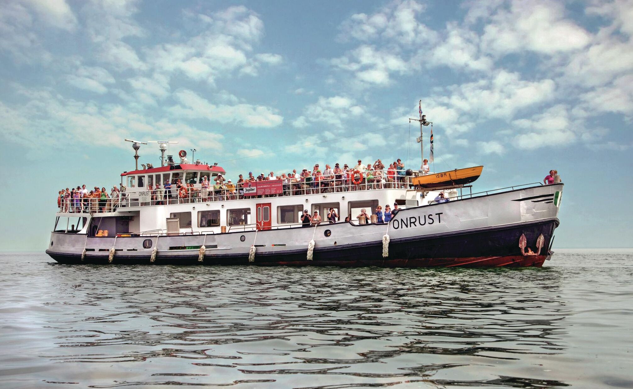 A ferry with multiple decks and passengers, named "ONRUST," sailing on calm waters.