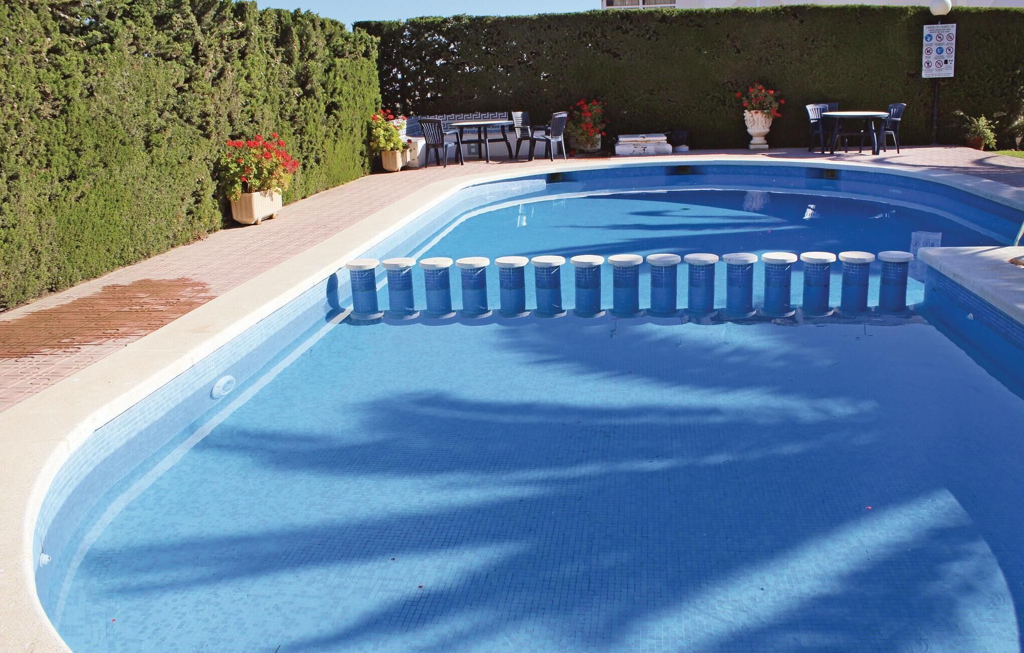 A swimming pool with a tiled deck, surrounded by potted plants and outdoor furniture.