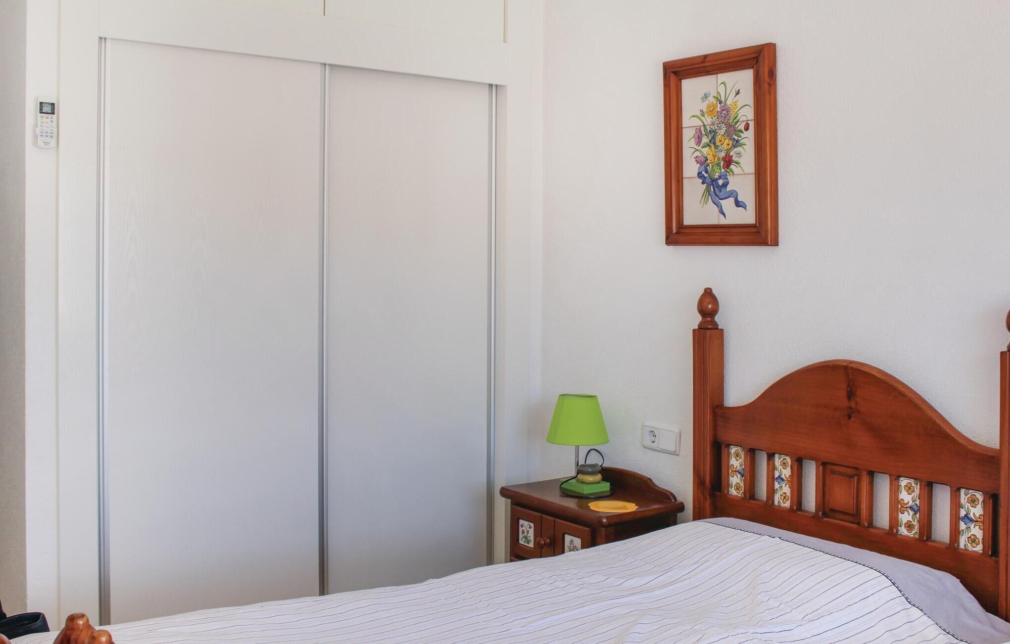 A bedroom with a bed, a nightstand with a lamp, a wardrobe, and a framed picture on the wall.