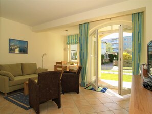 Ein Wohnzimmer mit einer Couch, Sesseln, einem Esstisch und Blick auf einen Garten durch eine Glastür.