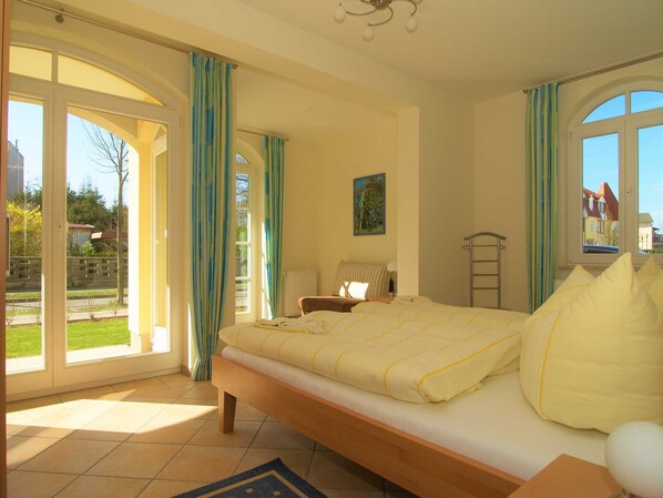 Une chambre à coucher avec un lit, un radiateur, une fenêtre avec des rideaux et une vue sur l’extérieur.