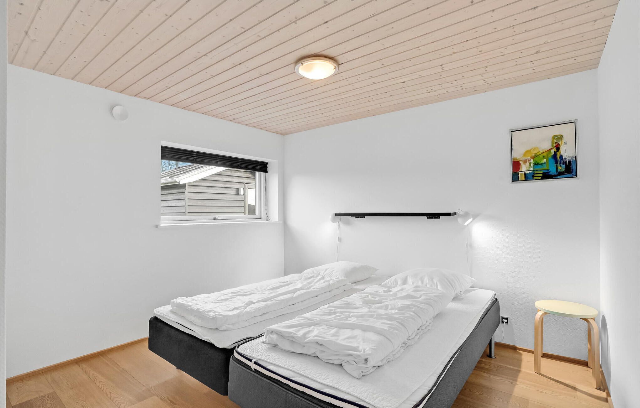 Et soveværelse med seng, et vindue, et natbord og en lampe monteret på væggen.