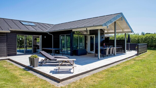 Et moderne hus med en overdækket terrasse, swimmingpool og en træterrasse.