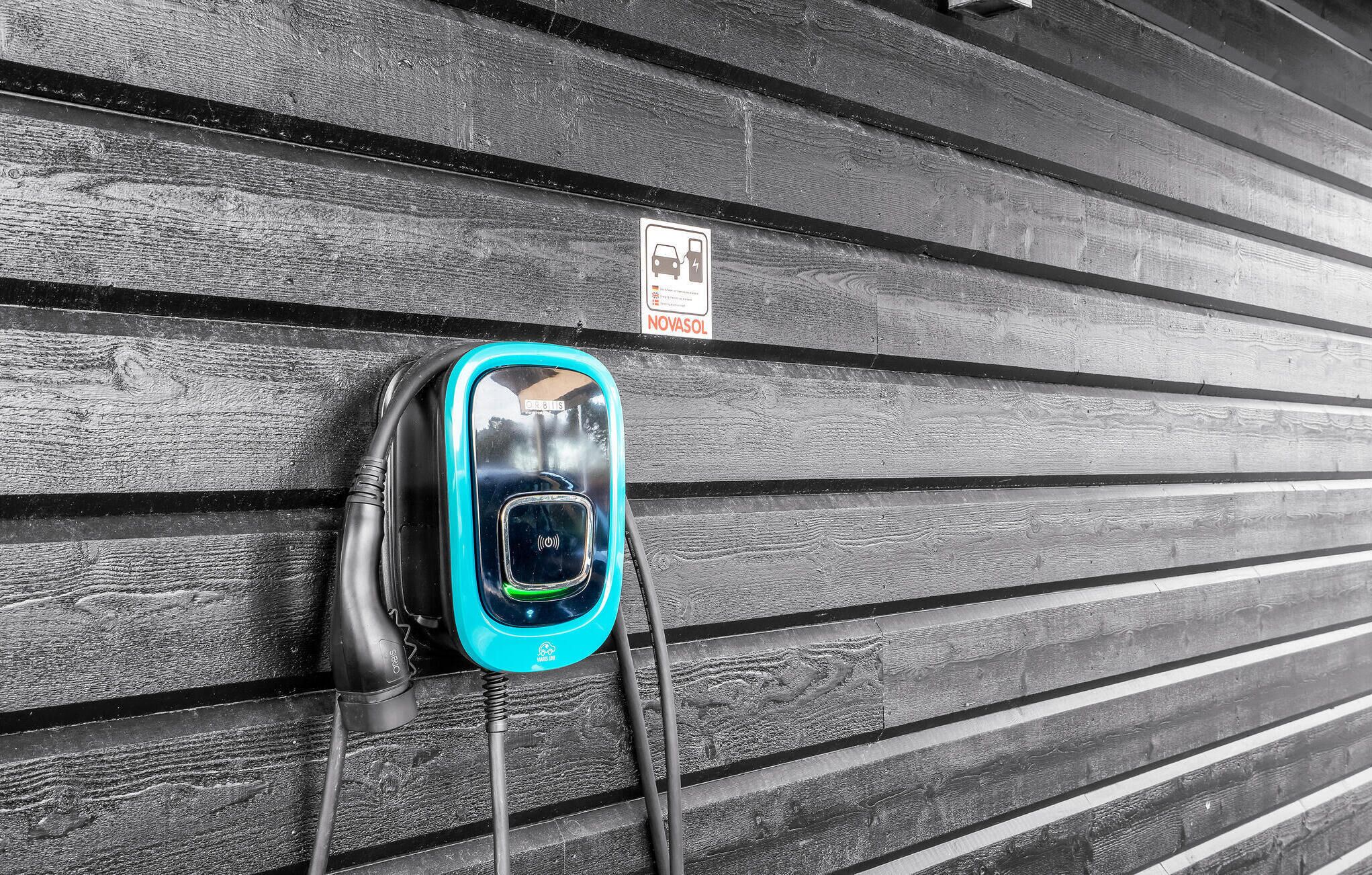 An electric vehicle charging station mounted on a wooden wall with a sign indicating it is Novasol.