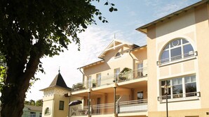 Um hotel de vários andares com varandas, uma estrutura semelhante a uma torre e um conjunto de sebes bem cuidado.