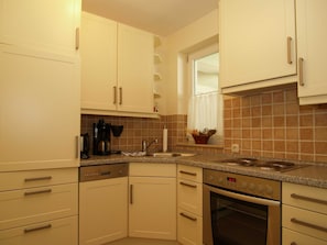 A kitchen with white cabinets, a built-in oven, a coffee maker, and a window with a curtain. - LG-08 - Residenz Lindengarten Whg. LG-08th (Kühlungsborn)