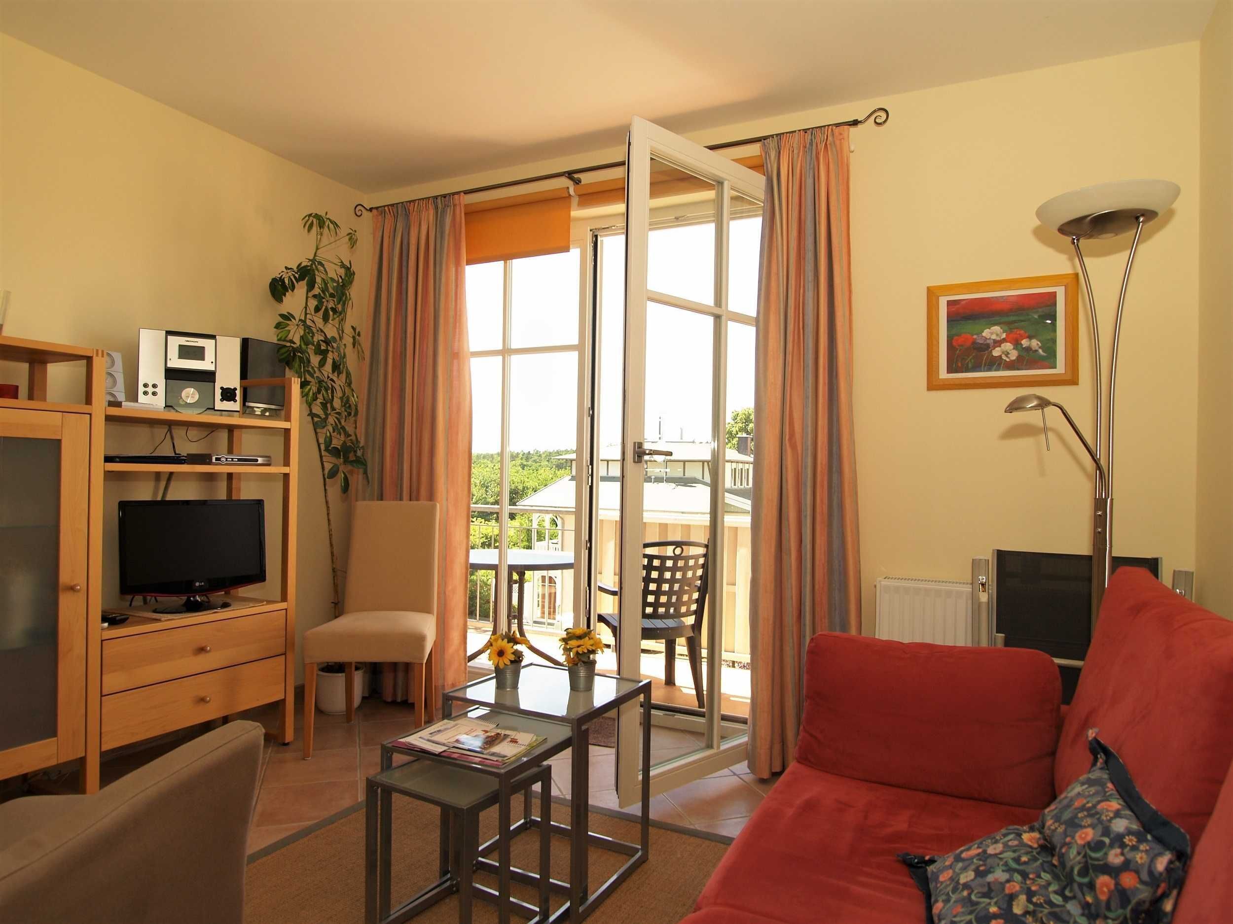 Un salon avec un canapé rouge, un téléviseur, une bibliothèque et un balcon donnant sur un paysage verdoyant.