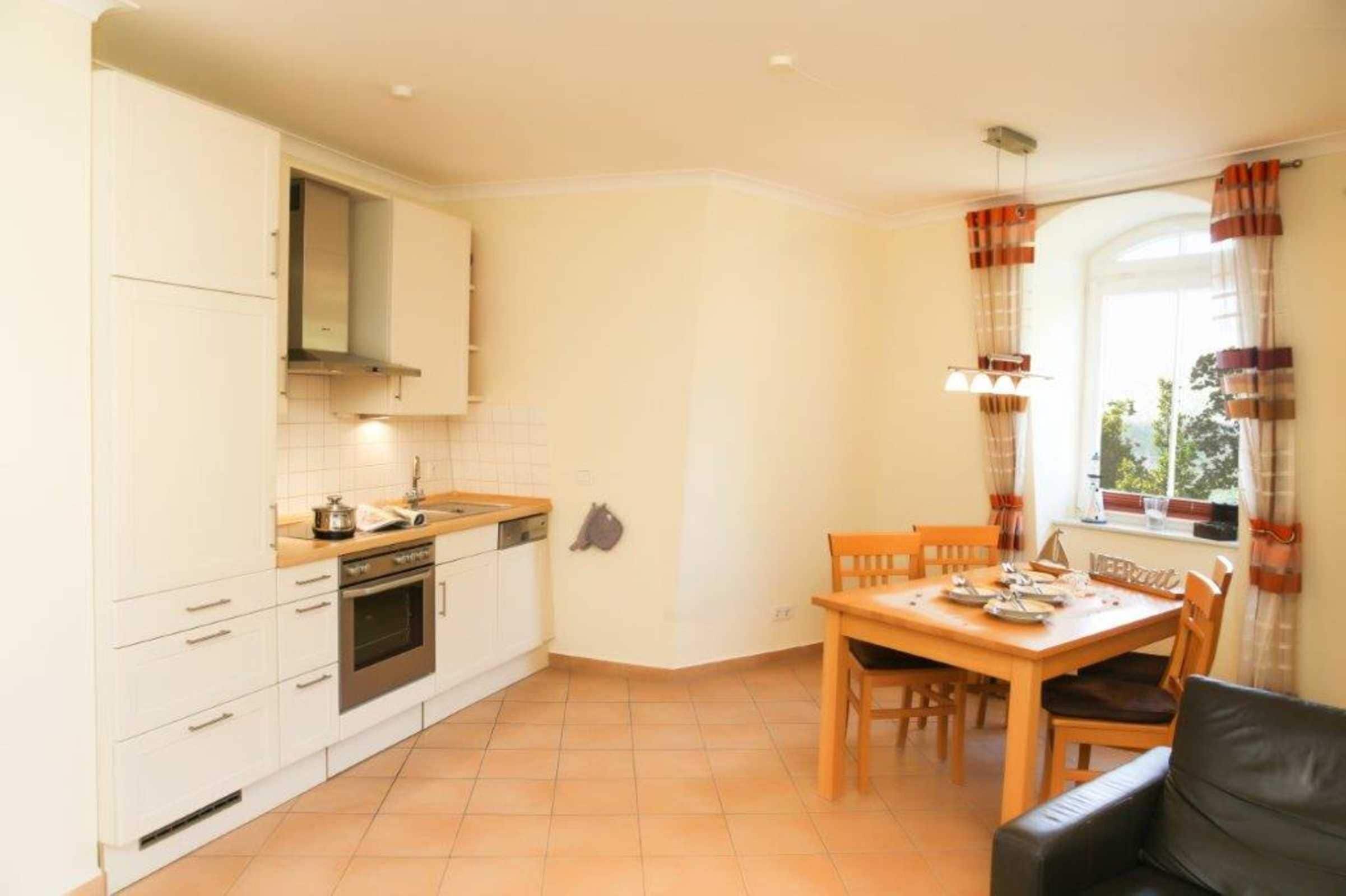 A compact kitchen with white cabinets, a stove, and a dining area with a table and chairs.