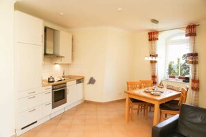 A compact kitchen with white cabinets, a stove, and a dining area with a table and chairs.