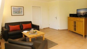 A living room with a black sofa, a wooden coffee table, and a television on a wooden cabinet. - (192) 2-room apartment lake view - Apartment house Baltic Sea beach (Kühlungsborn)