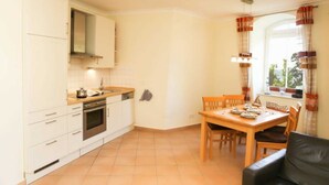 A compact kitchen with white cabinets, a stove, and a dining area with a table and chairs. - (192) 2-room apartment lake view - Apartment house Baltic Sea beach (Kühlungsborn)