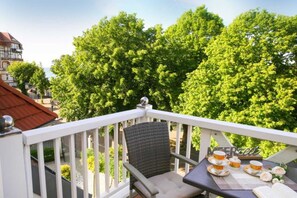 A balcony with a table set for tea, surrounded by lush green trees and a building in the background. - (192) 2-room apartment lake view - Apartment house Baltic Sea beach (Kühlungsborn)