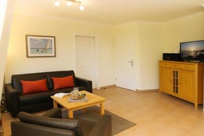 A living room with a black sofa, a wooden coffee table, and a television on a wooden cabinet. - (192) 2-room apartment lake view - Apartment house Baltic Sea beach (Kühlungsborn)