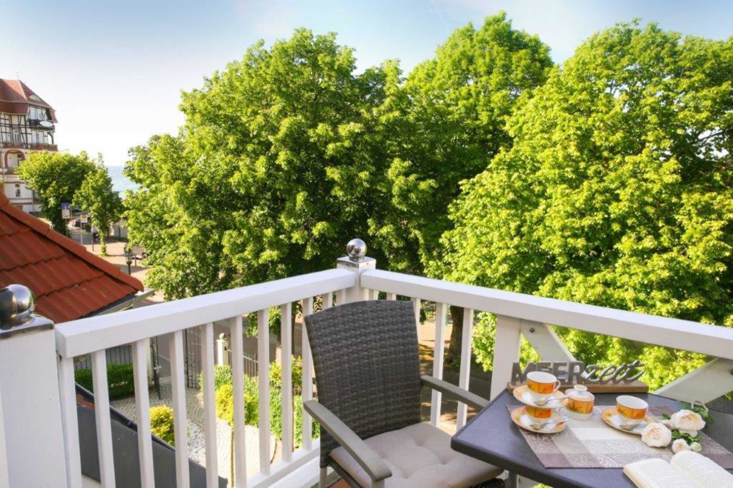 Een balkon met een gedekte tafel voor thee, omgeven door weelderige groene bomen en een gebouw op de achtergrond.
