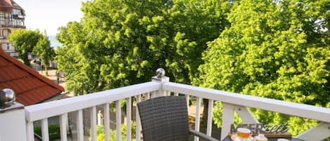 A balcony with a table set for tea, surrounded by lush green trees and a building in the background.