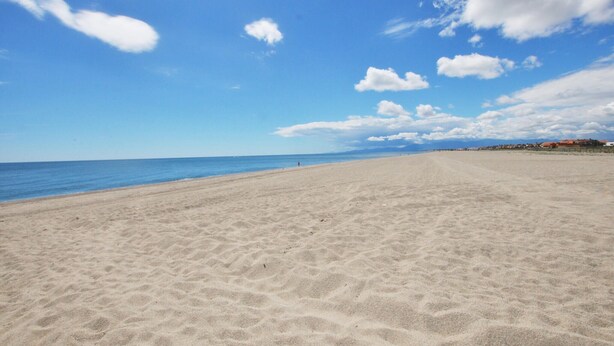 Une vaste plage de sable fin, sous un ciel bleu azur parsemé de quelques nuages.