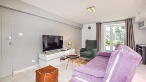 Un salon moderne avec un téléviseur à écran plat, un fauteuil vert, un canapé violet et un pouf en cuir.
