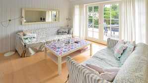A cozy living room with a floral-patterned sofa, a striped armchair, a small table with a floral tablecloth, and a large window with curtains. - Gorgeous home in Sydals with WiFi (Sydals)
